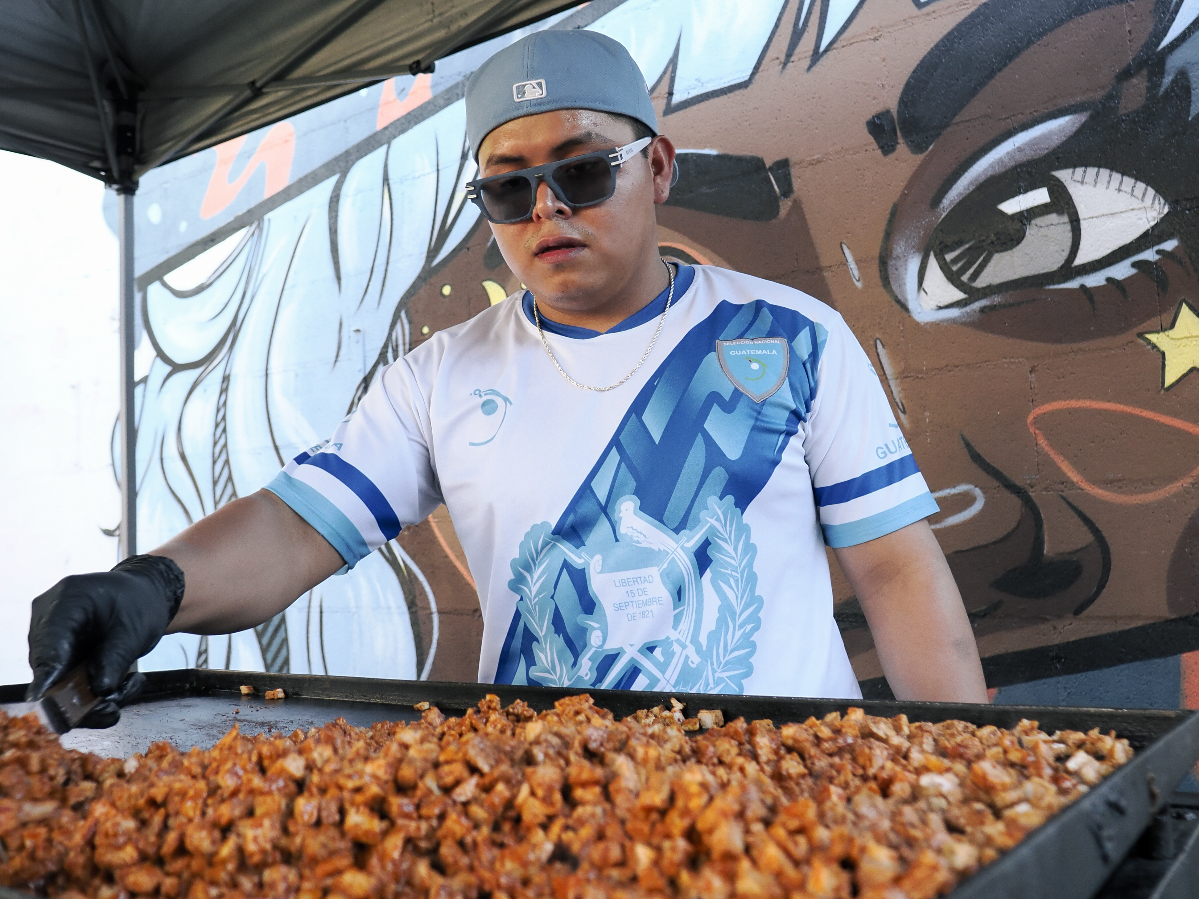 Vendor in a Guatemala jersey working the grill in front of the court mural