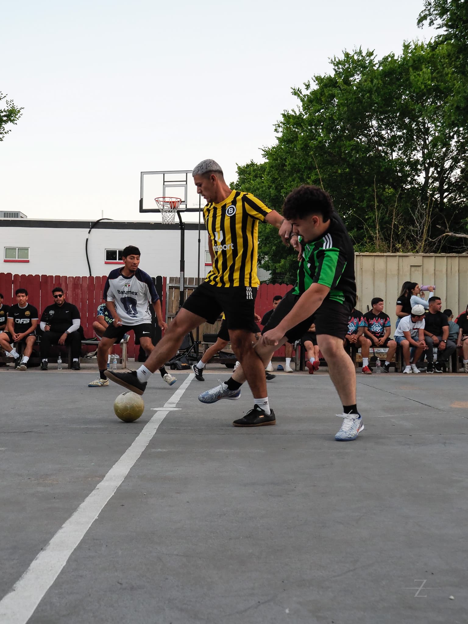 Two players fighting for the ball in front of the graffiti-covered container wall