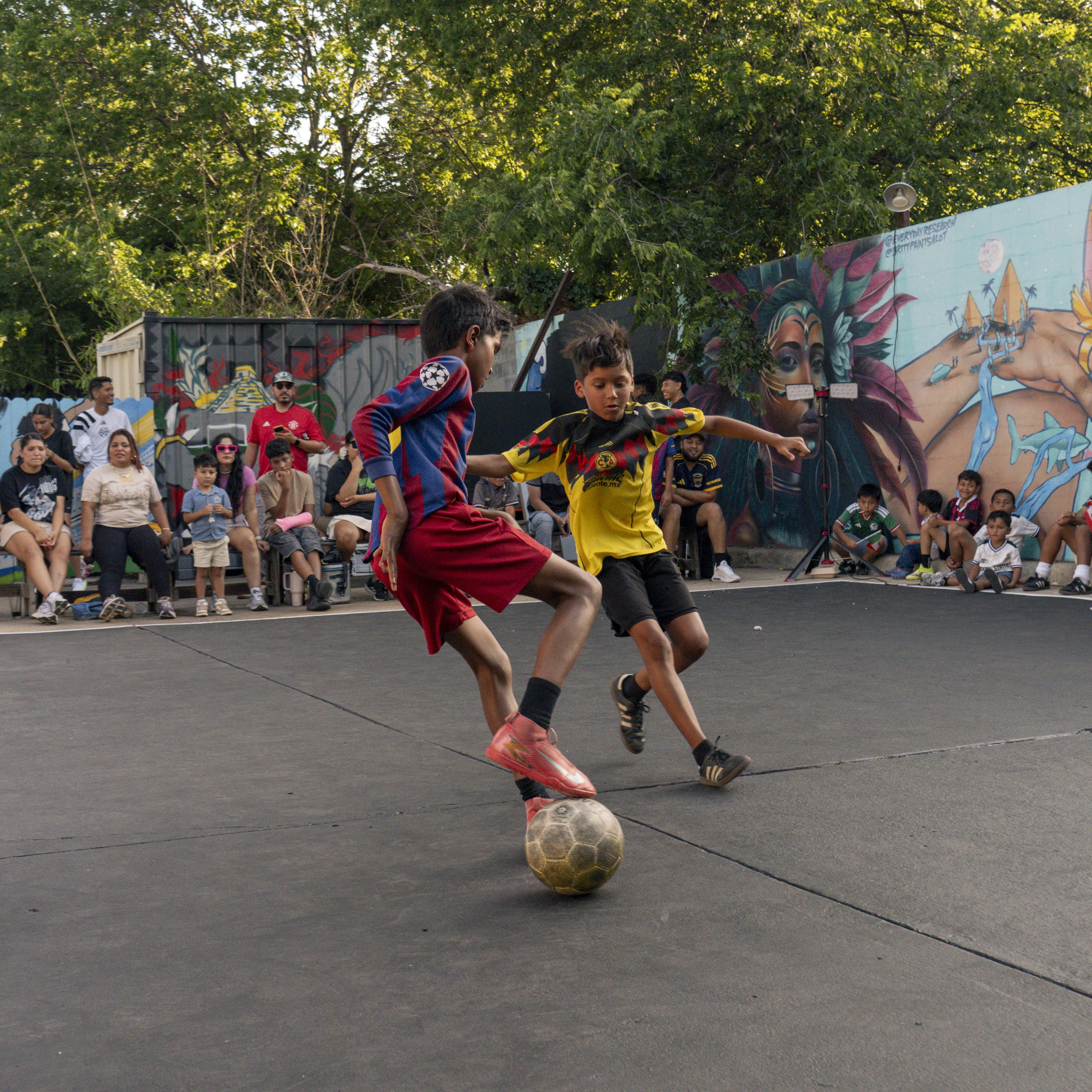 Two kids going toe to toe for the ball on the mural-lined court